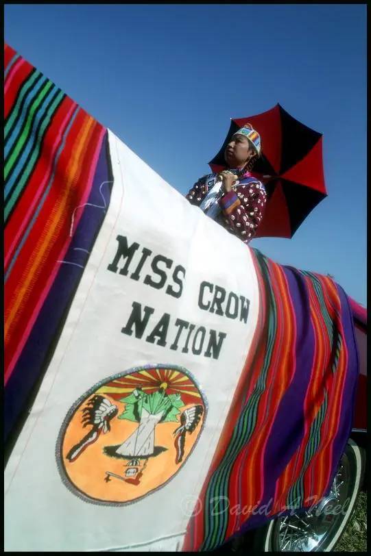 Miss Crow Nation stays out of the sun as she rides in a parade at Crow Fair.