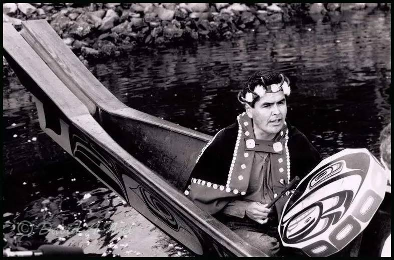 Robert Davidson singing with a hand drum in Bill Reid's canoe.
